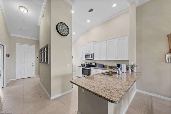 Kitchen featuring white cabinetry, stainless steel appliances, a double basin sink, and a spacious breakfast bar with a stone-finish countertop