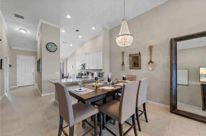 Open-concept dining area featuring a crystal chandelier, tiled flooring, vaulted ceiling, and crown molding