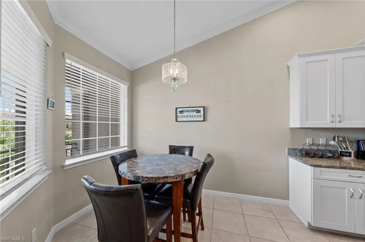 Vaulted ceiling dining area featuring a crystal chandelier, large window with blinds, tiled flooring, white cabinetry, and a granite countertop