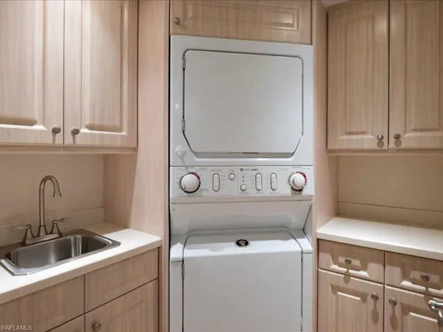 Clothes washing area featuring cabinets, sink, and stacked washing maching and dryer