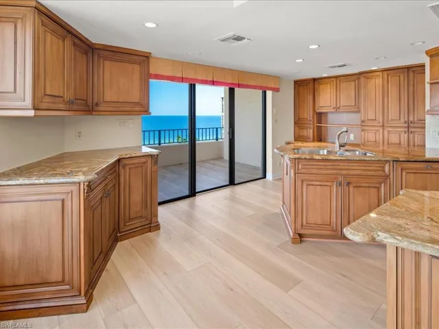 Kitchen featuring light stone counters, an island with sink, sink, light hardwood / wood-style flooring, and a water view