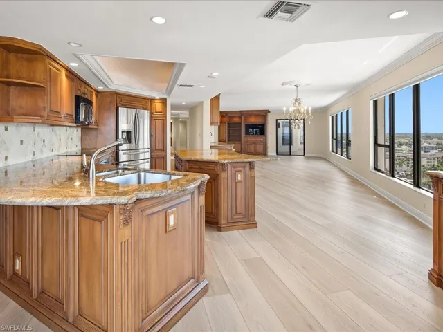 Kitchen featuring an inviting chandelier, stainless steel refrigerator with ice dispenser, a kitchen island with sink, and light wood-type flooring