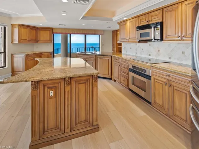 Kitchen with stainless steel appliances, kitchen peninsula, a raised ceiling, and light wood-type flooring