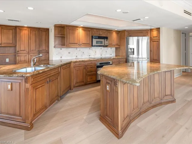 Kitchen with light stone countertops, an island with sink, appliances with stainless steel finishes, and sink