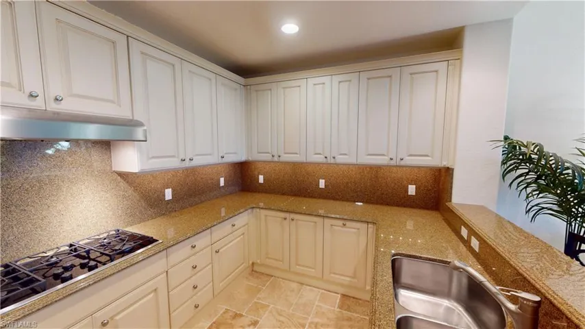 Kitchen with stainless steel gas stovetop, sink, backsplash, and light stone counters