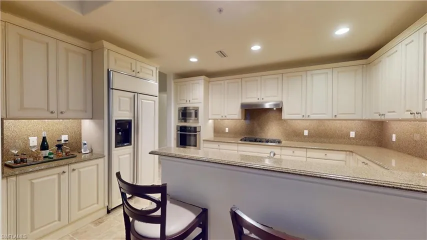 Kitchen featuring visible vents, backsplash, light stone countertops, under cabinet range hood, and built in appliances