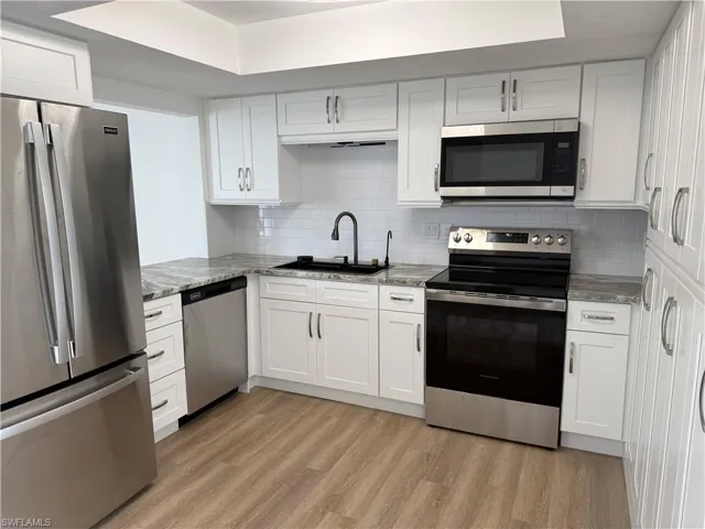 Kitchen featuring stainless steel appliances, white cabinets, light stone counters, and light wood finished floors