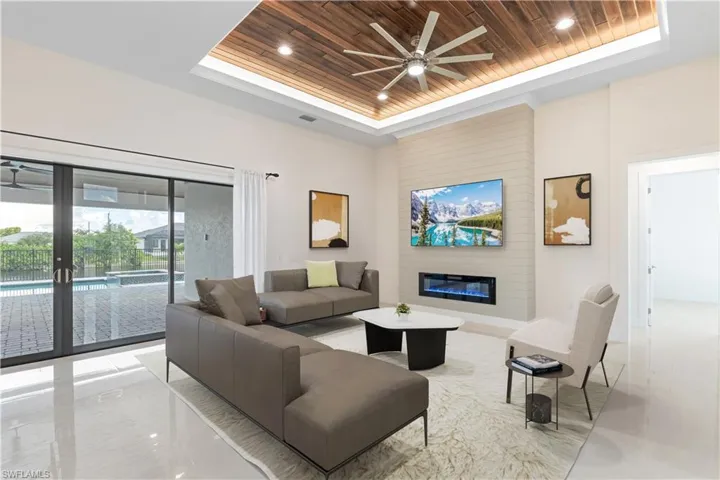 Living room with a ceiling fan, a tray ceiling, wooden ceiling, a large fireplace, and recessed lighting