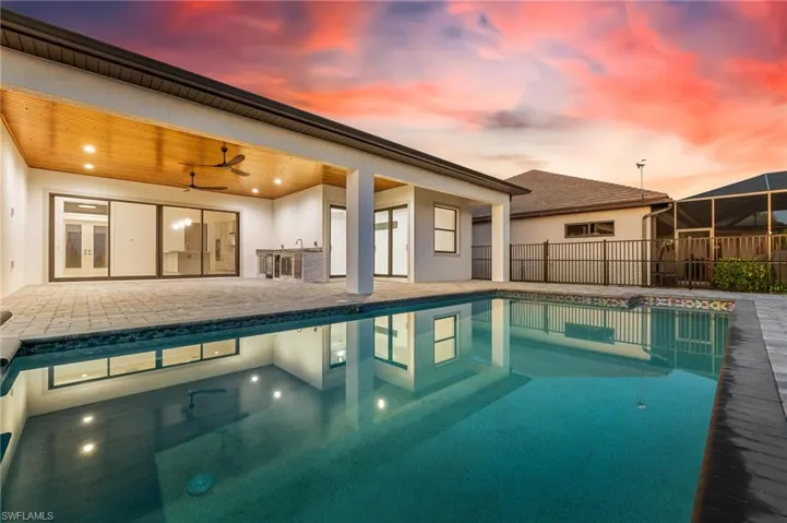 Pool at dusk with a patio, a ceiling fan, and an outdoor kitchen