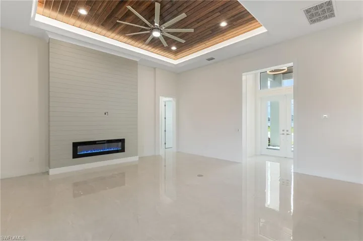 Unfurnished living room with a tray ceiling, wooden ceiling, a large fireplace, a ceiling fan, and french doors