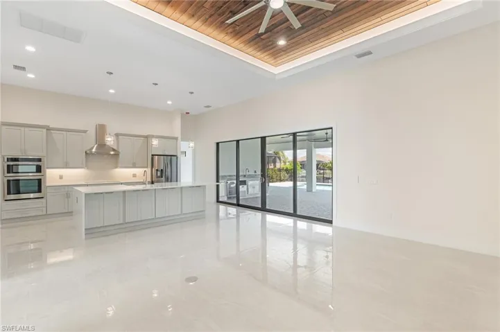 Kitchen featuring a tray ceiling, wooden ceiling, a kitchen island with sink, decorative light fixtures, and gray cabinets