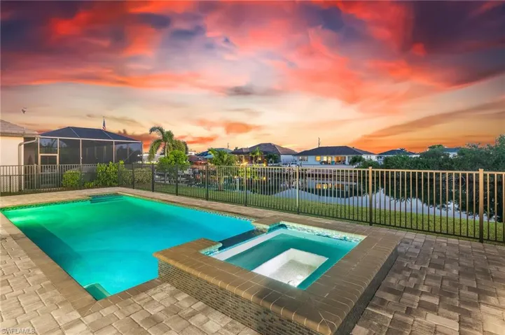 Pool at dusk with a patio, a water view, a pool with connected hot tub, and a fenced backyard