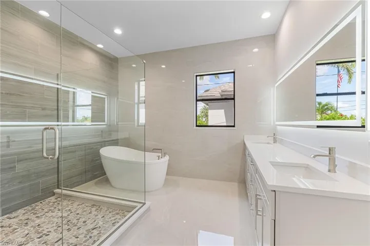Bathroom featuring double vanity, a freestanding tub, a shower stall, recessed lighting, and tile walls