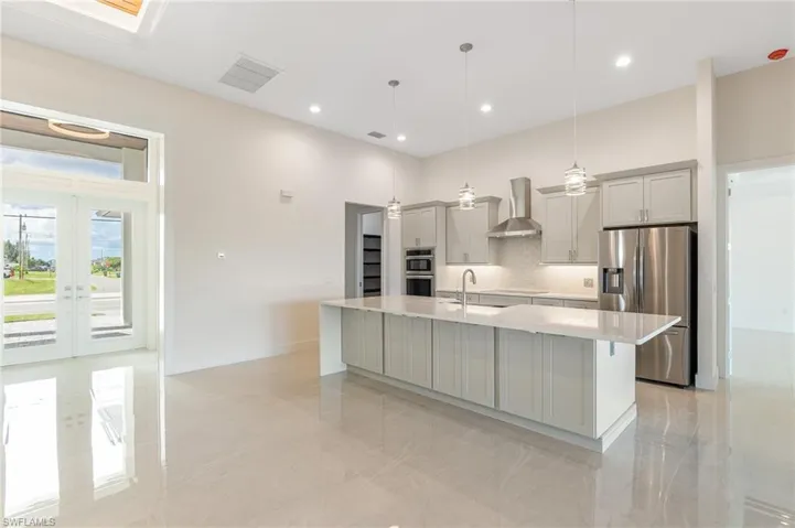 Kitchen with decorative backsplash, appliances with stainless steel finishes, decorative light fixtures, a spacious island, and wall chimney range hood