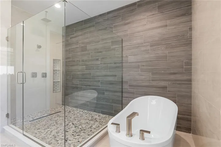 Bathroom featuring a soaking tub, a stall shower, and tile walls