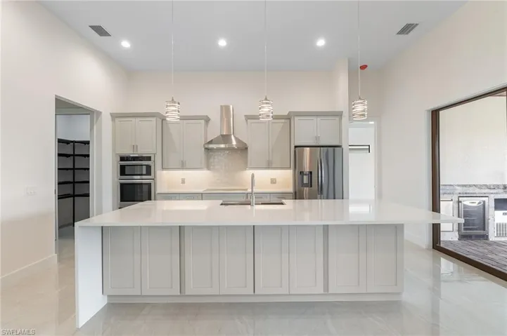 Kitchen with backsplash, light stone counters, gray cabinets, wall chimney exhaust hood, and stainless steel appliances