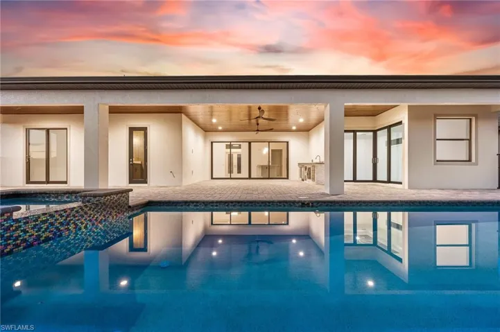 Pool at dusk with a patio, ceiling fans and outdoor kitchen