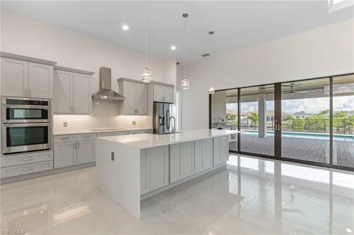 Kitchen featuring pendant lighting, decorative backsplash, an island with sink, gray cabinetry, and light stone counters