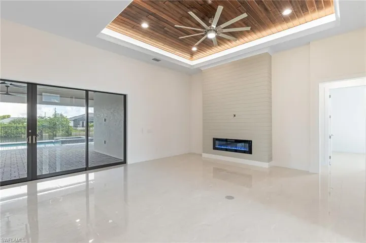 Unfurnished living room featuring ceiling fan, a raised ceiling, wooden ceiling, and a large fireplace