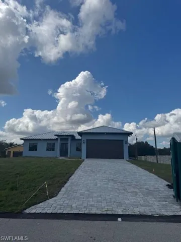 Prairie-style house with a front yard, a garage, decorative driveway, a metal roof, and stucco siding
