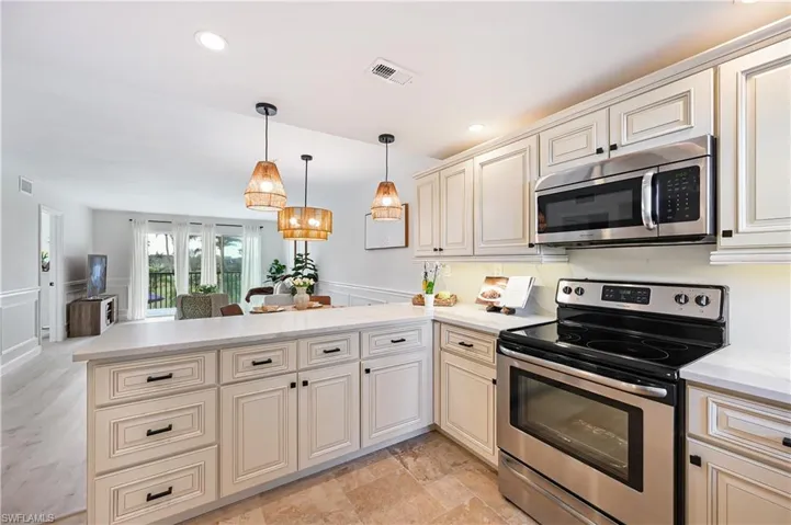 Kitchen with cream cabinetry, stainless steel appliances, decorative backsplash, a peninsula, and hanging light fixtures