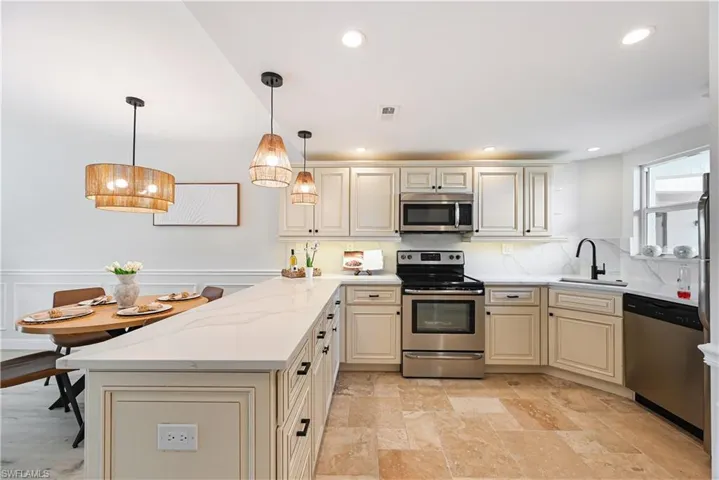Kitchen with cream cabinets, stainless steel appliances, a peninsula, backsplash, and a wainscoted wall