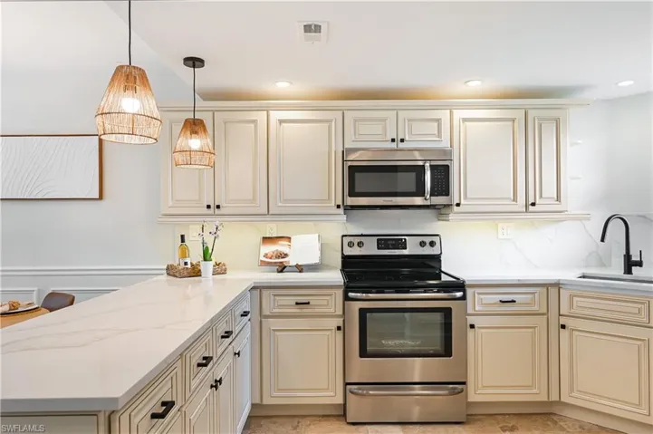 Kitchen with cream cabinets, stainless steel appliances, a wainscoted wall, a peninsula, and open floor plan