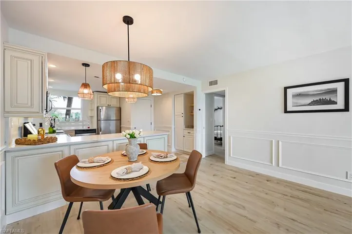 Dining area with light wood-type flooring, a decorative wall, wainscoting, and hanging lights