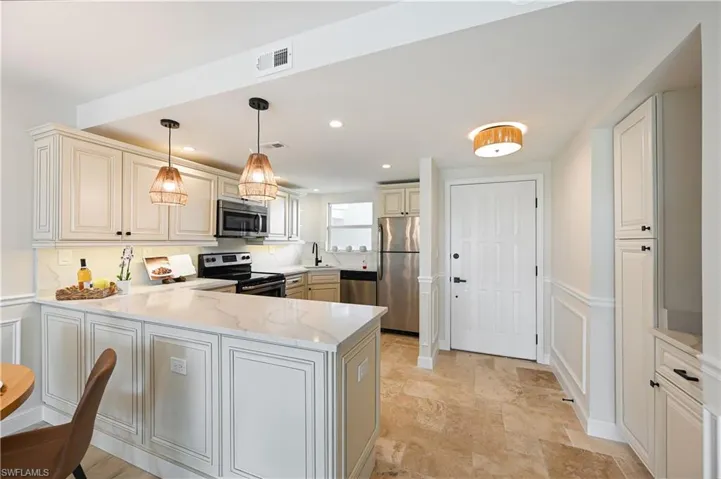 Kitchen featuring a wainscoted wall, stainless steel appliances, a decorative wall, cream cabinetry, and a peninsula