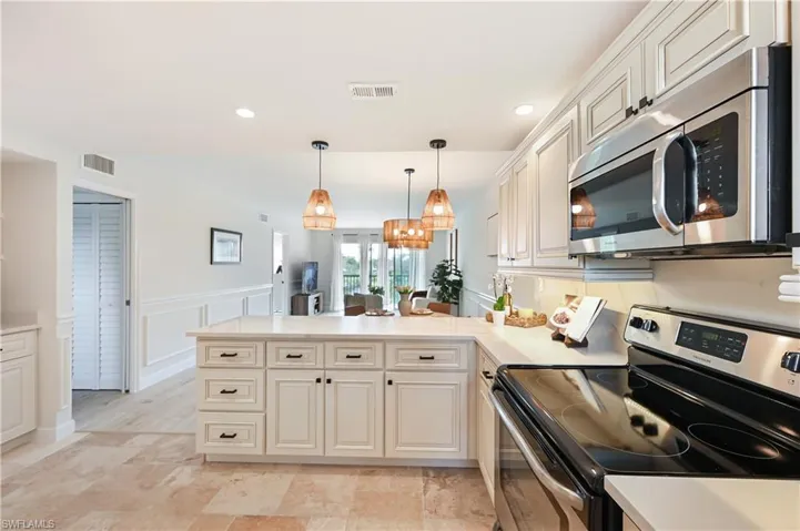 Kitchen featuring stainless steel appliances, light countertops, a peninsula, a wainscoted wall, and a decorative wall