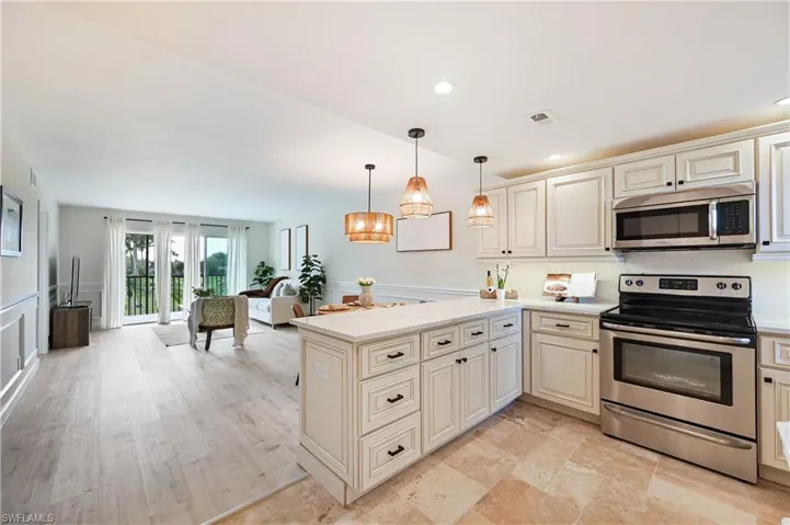 Kitchen with stainless steel appliances, cream cabinetry, open floor plan, a wainscoted wall, and a decorative wall