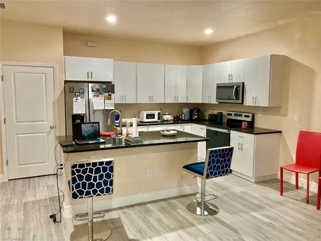 Kitchen with a kitchen breakfast bar, appliances with stainless steel finishes, light hardwood / wood-style floors, kitchen peninsula, and white cabinets