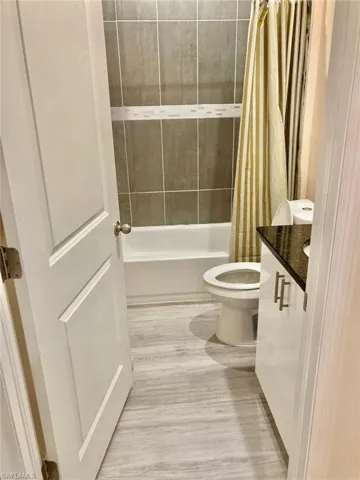 Full bathroom with vanity, toilet, wood-type flooring, and shower / bathtub combination with curtain