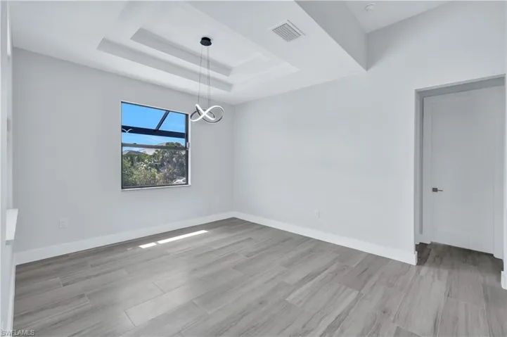 Empty room featuring a tray ceiling, wood finished floors, baseboards, visible vents, and an inviting chandelier
