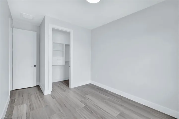 Unfurnished bedroom with a closet, visible vents, baseboards, wood finished floors, and attic access