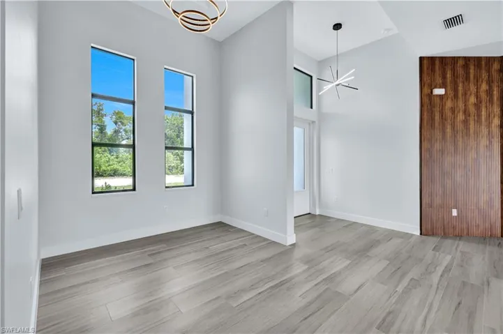 Unfurnished room featuring light wood-style flooring, visible vents, baseboards, a high ceiling, and an inviting chandelier