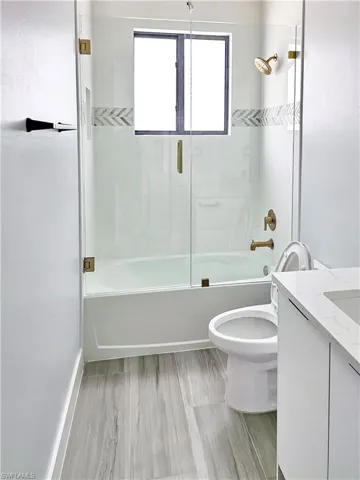 Bathroom with enclosed tub / shower combo, toilet, and vanity