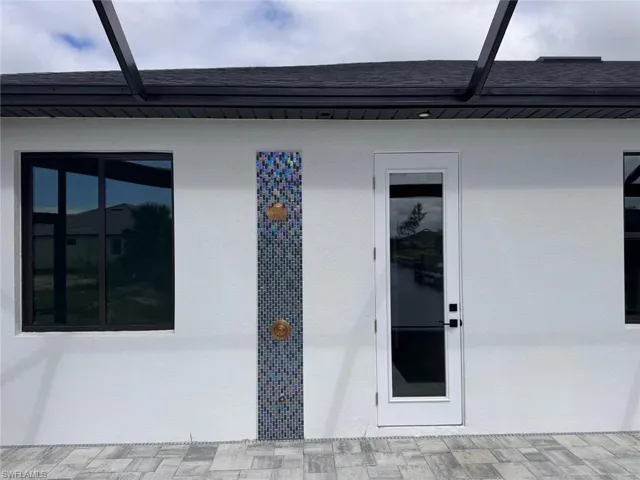Doorway to property with a shingled roof and stucco siding