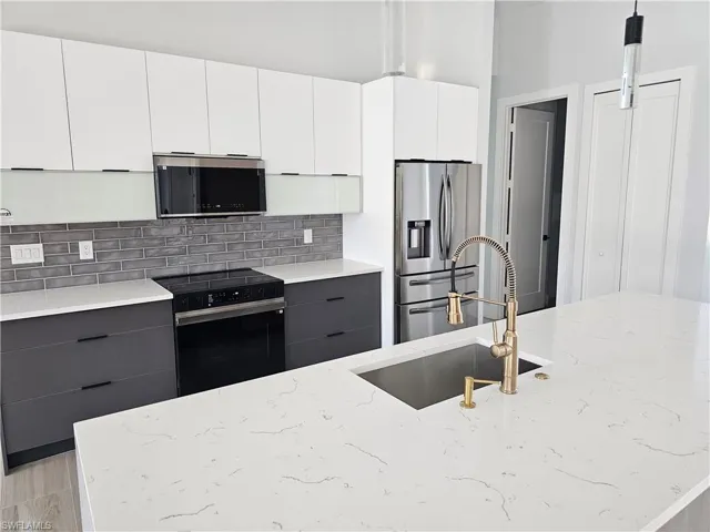Kitchen with electric range, a sink, gray cabinets, backsplash, and stainless steel fridge with ice dispenser
