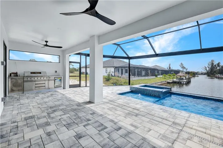 View of pool featuring a water view, exterior kitchen, glass enclosure, a patio, and ceiling fan