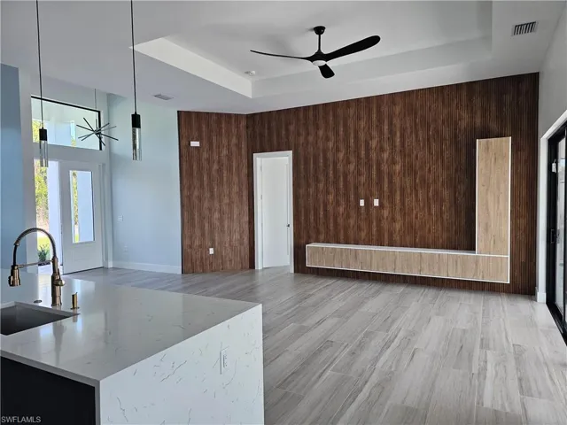 Living room featuring ceiling fan, wood walls, visible vents, light wood-type flooring, and a raised ceiling