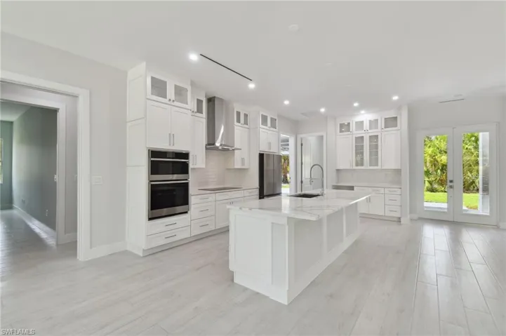 Kitchen featuring wall chimney range hood, white cabinets, backsplash, and stainless steel appliances