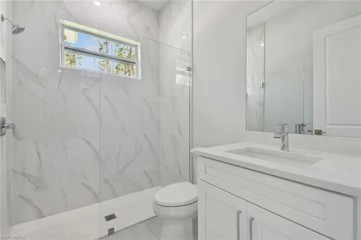 Bathroom with a tile shower, tile flooring, oversized vanity, and toilet