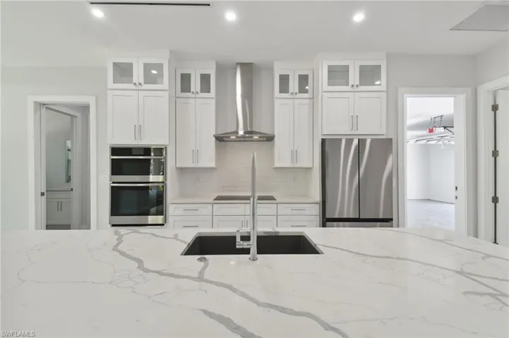 Kitchen featuring wall chimney range hood, white cabinets, light stone counters, and stainless steel appliances
