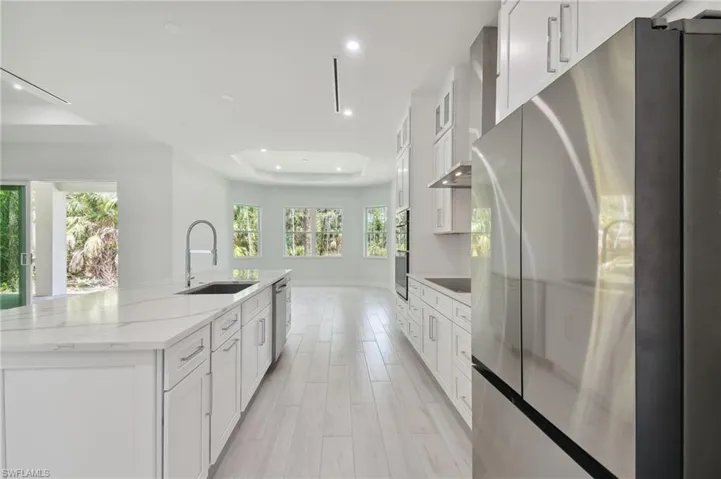 Kitchen with a tray ceiling, sink, white cabinets, a kitchen island with sink, and appliances with stainless steel finishes