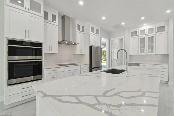 Kitchen with appliances with stainless steel finishes, wall chimney range hood, and white cabinetry