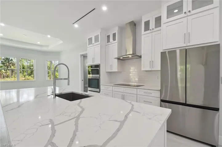 Kitchen with light stone countertops, stainless steel appliances, wall chimney exhaust hood, sink, and white cabinetry