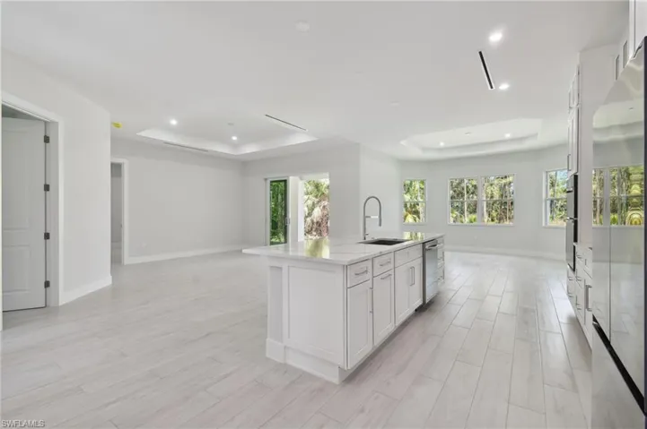 Kitchen featuring stainless steel appliances, a raised ceiling, a kitchen island with sink, white cabinetry, and sink
