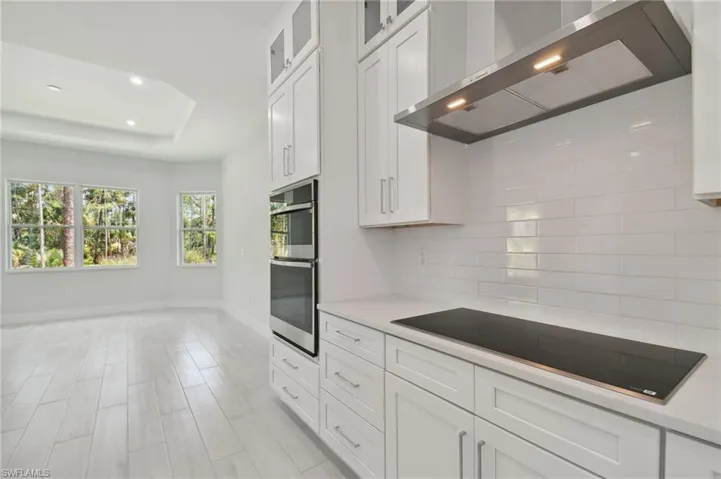 Kitchen with backsplash, black electric cooktop, wall chimney exhaust hood, white cabinets, and stainless steel double oven