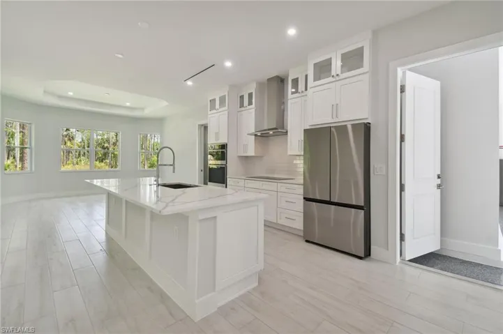 Kitchen featuring wall chimney range hood, stainless steel appliances, a center island with sink, a raised ceiling, and sink